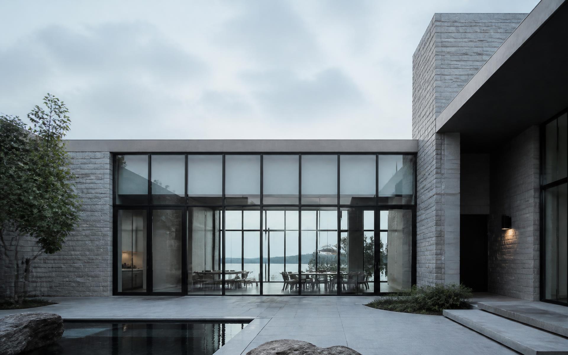 Sunlit interior with floor-to-ceiling slim-profile steel windows opening onto a stone terrace