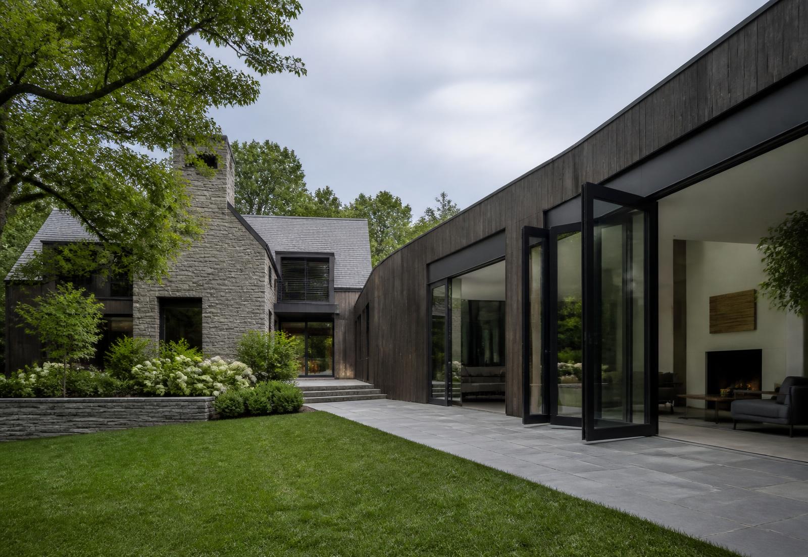 Contemporary Greenwich residence with folding black steel doors opening from a living room to a lawn and terrace
